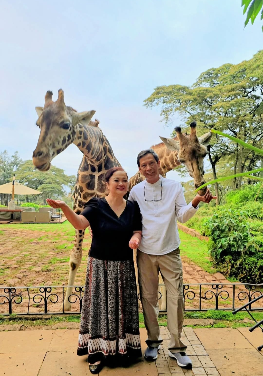 Dr. Irene and Dr. Nilo with giraffes in a green outdoor setting.